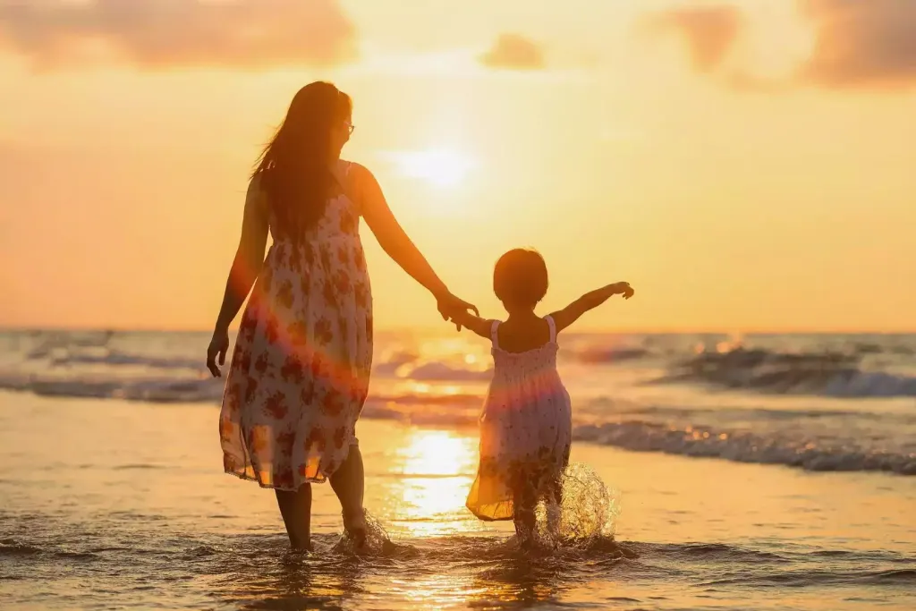 Madre e hija de la mano durante la puesta de sol en la playa
