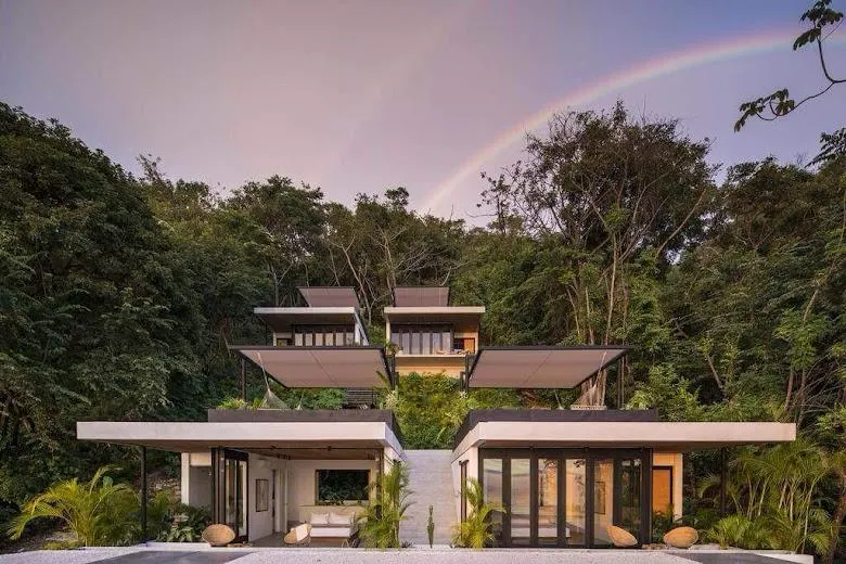 Hotel Mint — stepped pavilions with white roof canopies against the Santa Teresa jungle, a rainbow overhead.